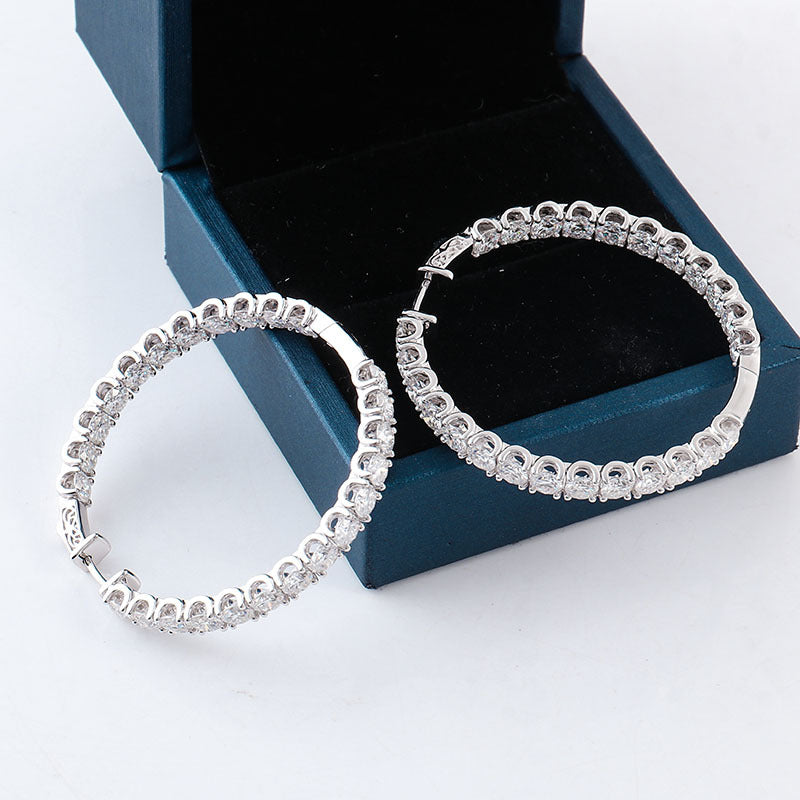 Silver hoop earrings on a white surface with a blue jewelry box in the background.
