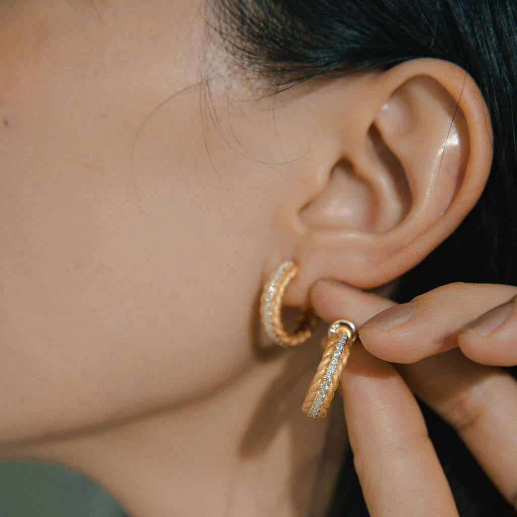 Close-up of an ear wearing a gold hoop earring with a blurred background