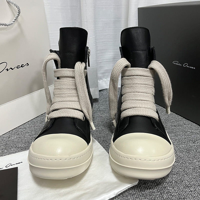 Black high-top sneakers with white soles on a gray surface, with a branded box in the background.