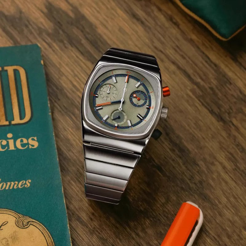 Silver wristwatch on a wooden surface with a book and pen