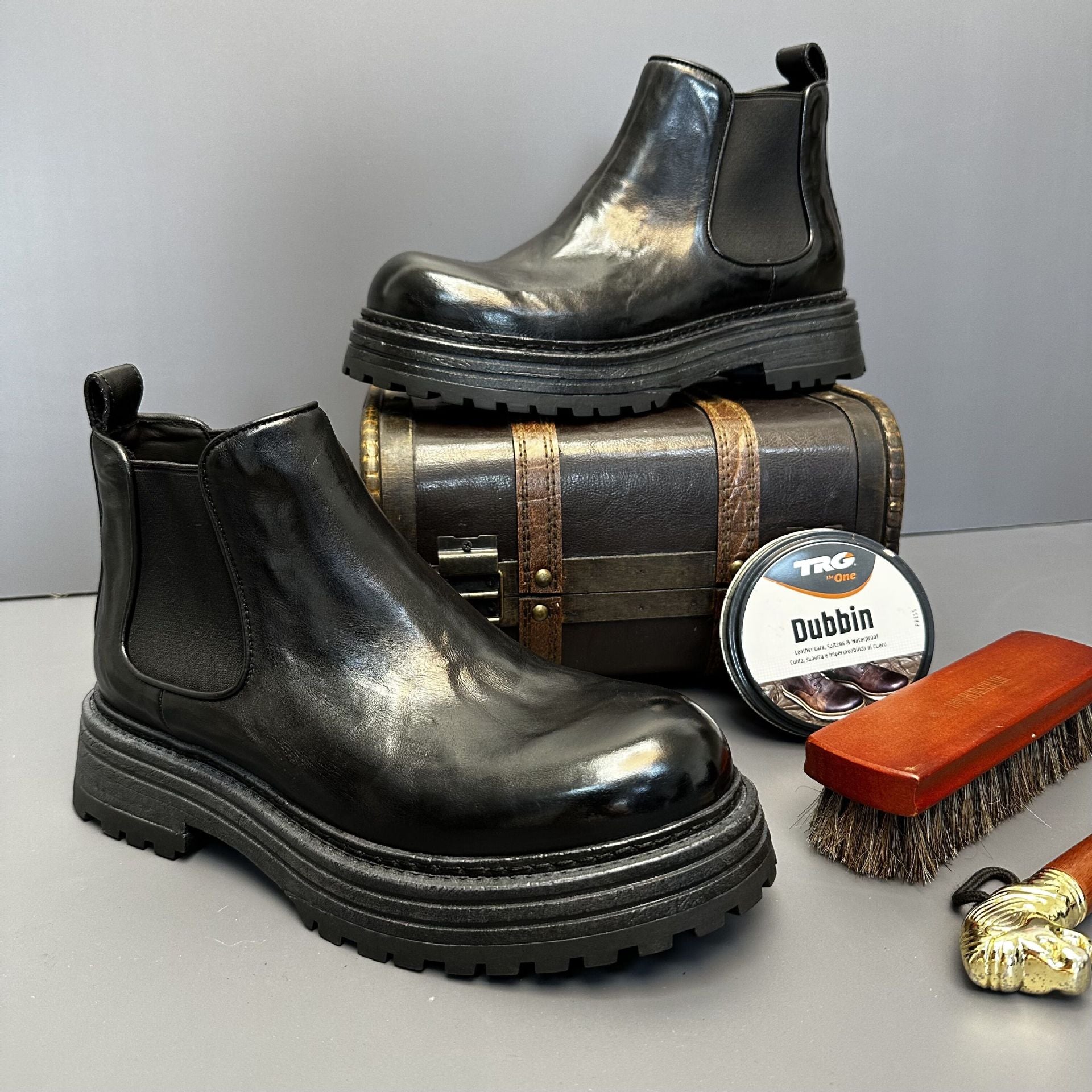 Black leather boots with a barrel, TRQ Dubbin container, and brush on a light gray background