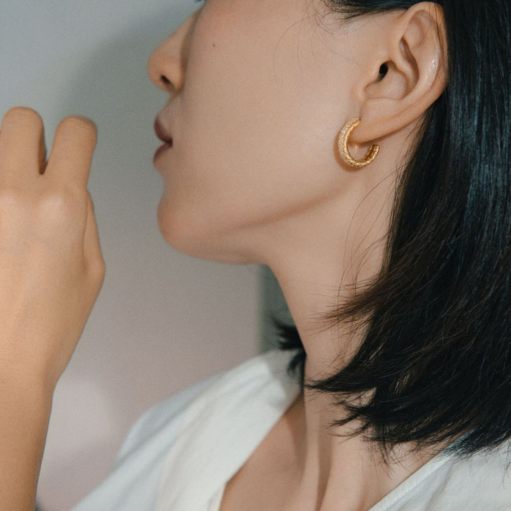 Close-up of a person wearing gold hoop earrings with a neutral background