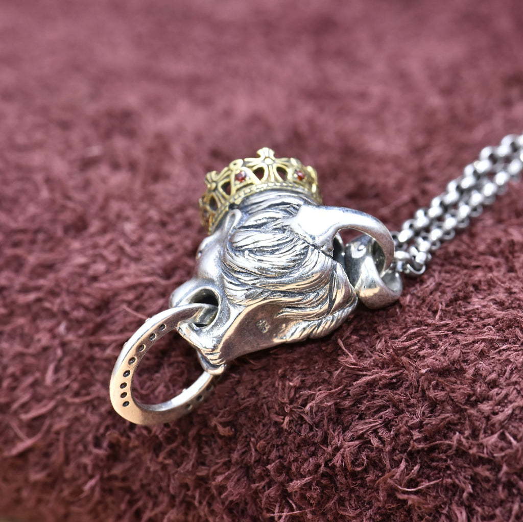 Silver lion pendant with a gold crown on a chain against a brown textured background