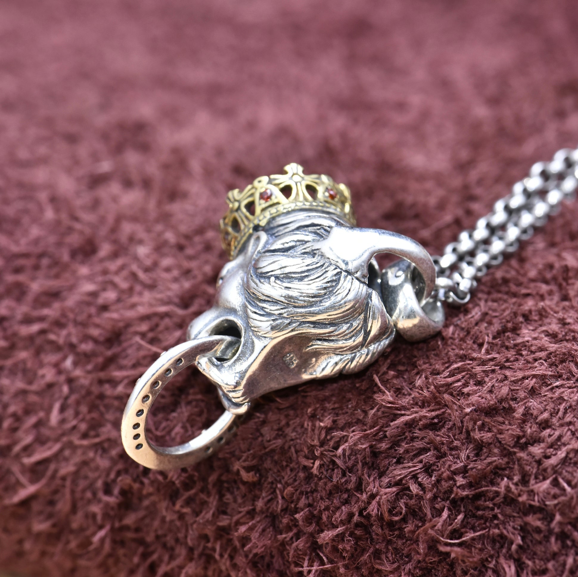 Silver lion pendant with a gold crown on a chain against a brown textured background