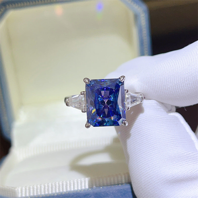 Blue gemstone ring held by a gloved hand with a blurred background