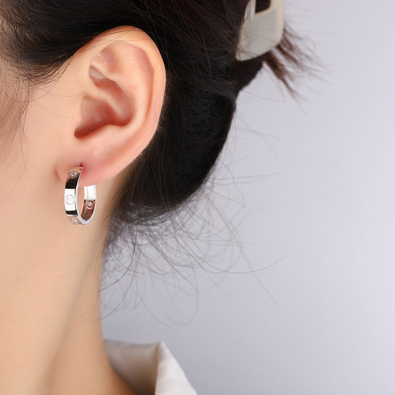 Close-up of an ear wearing a small hoop earring with a gray background
