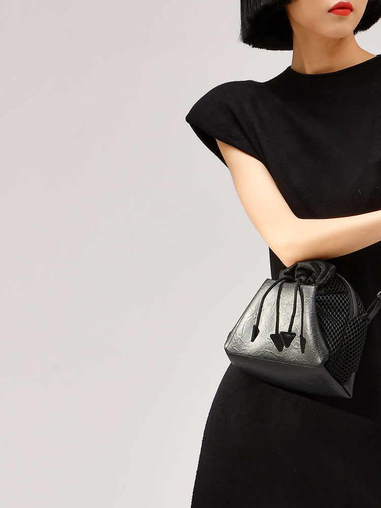 Person holding a black handbag with a textured pattern against a plain background