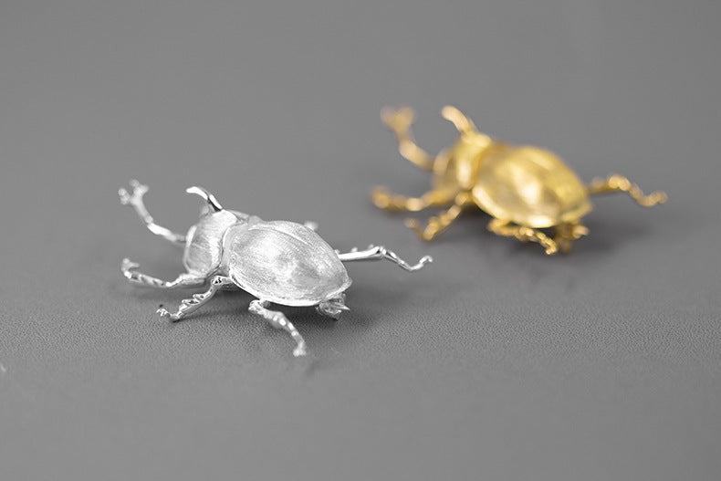 Silver and gold beetle-shaped objects on a gray background