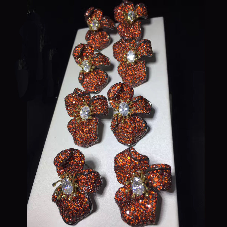 Pair of floral earrings with brown gemstones on a white stand against a black background
