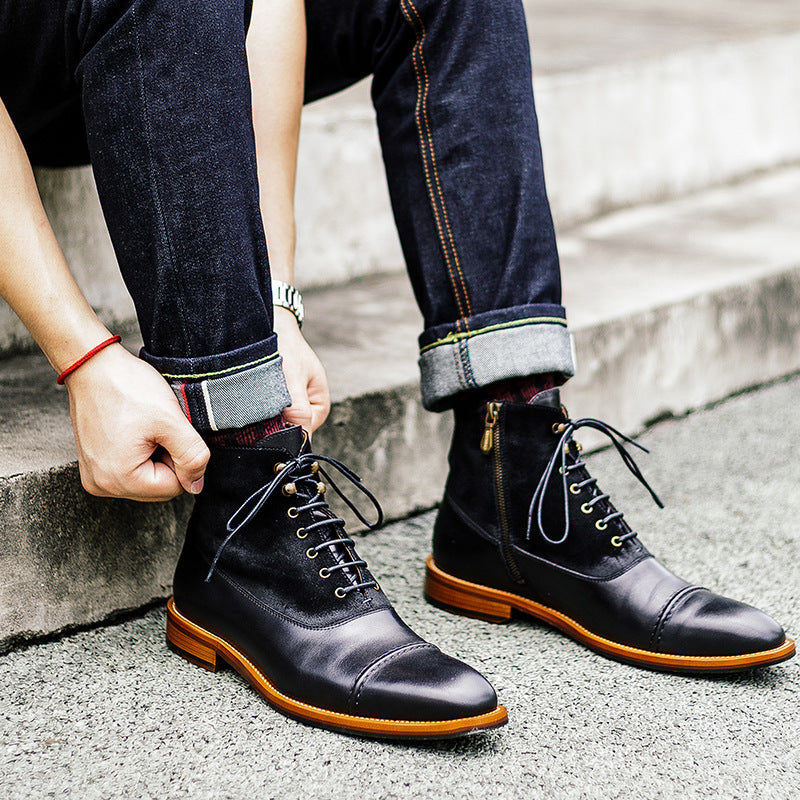 Person wearing black leather boots with orange soles, standing on a concrete surface.