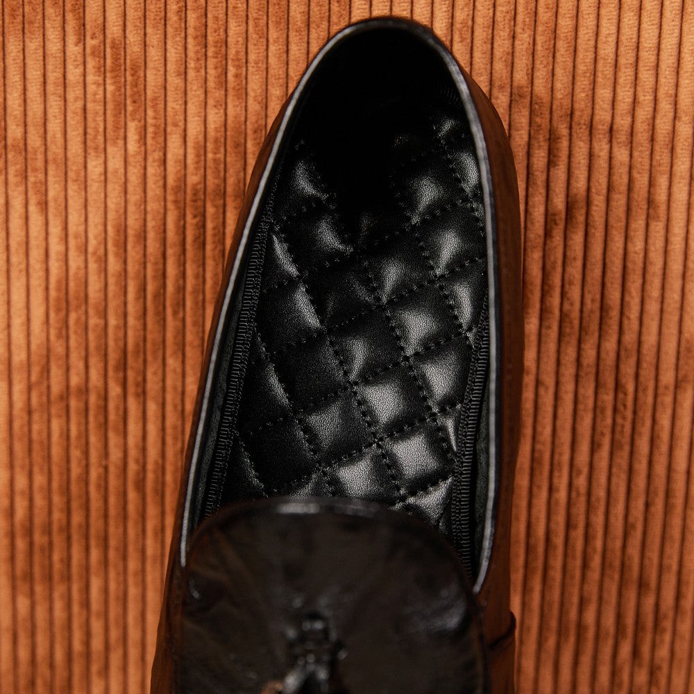 Black dress shoe with quilted design on a wooden surface