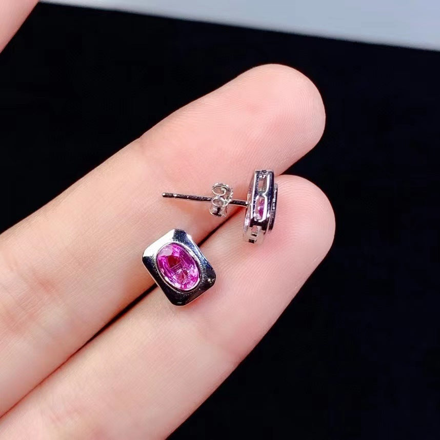 Silver earrings with pink gemstones held between fingers against a dark background