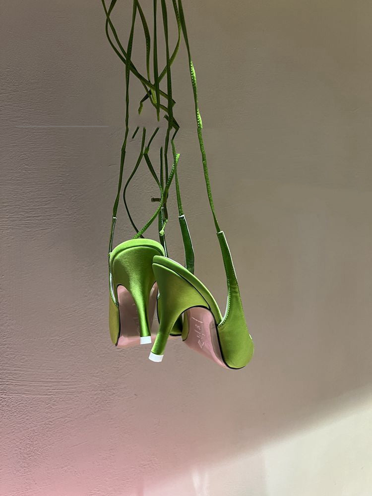 Green high-heeled shoes with pink soles hanging against a plain background