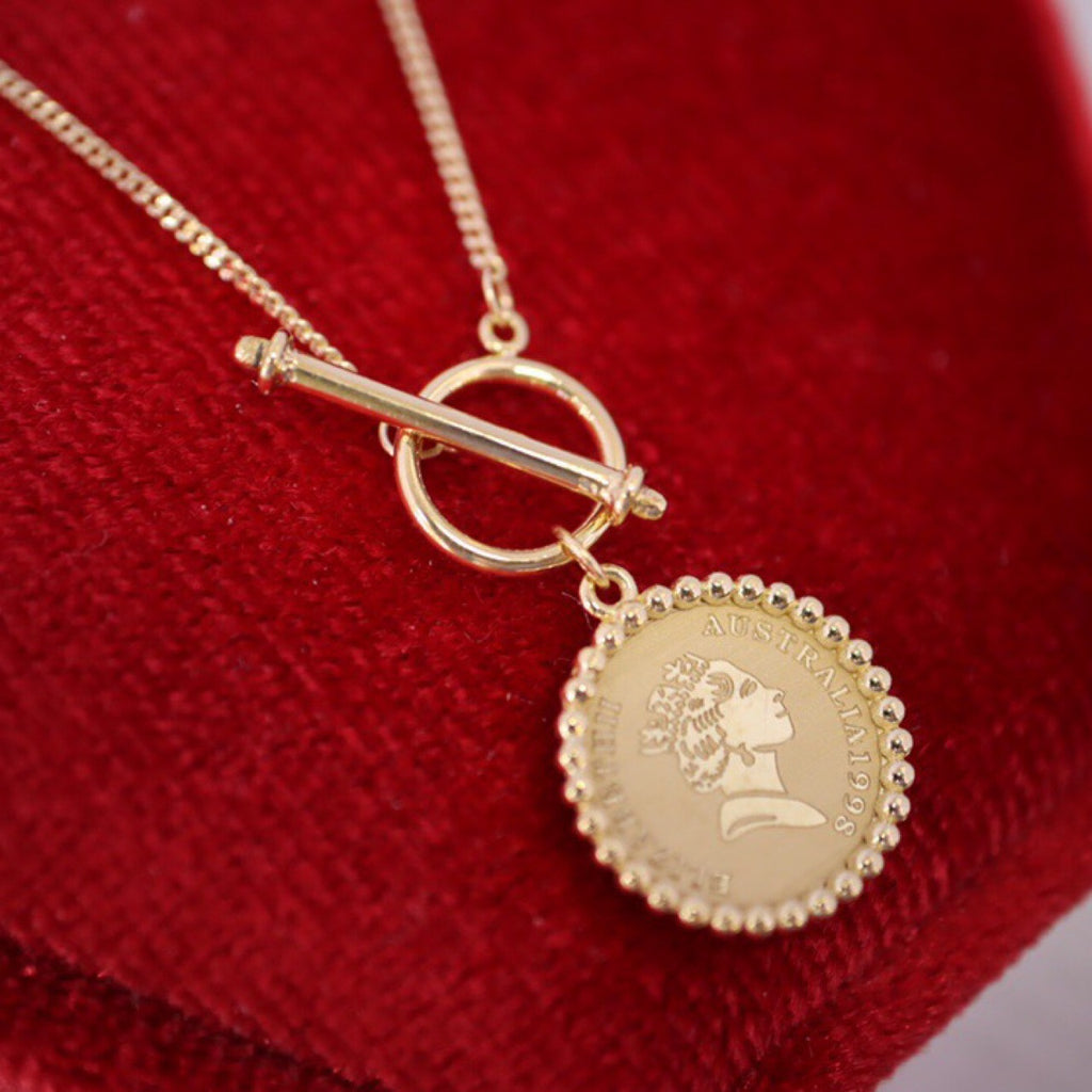 Gold necklace with a coin pendant on a red fabric background