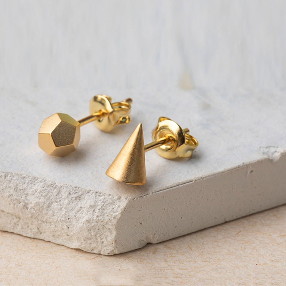 Gold geometric stud earrings on a light stone surface