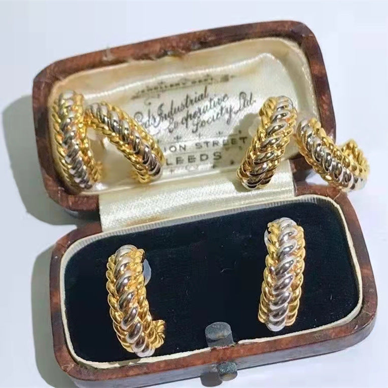 Pair of gold and silver twisted earrings in an open jewelry box with visible branding.