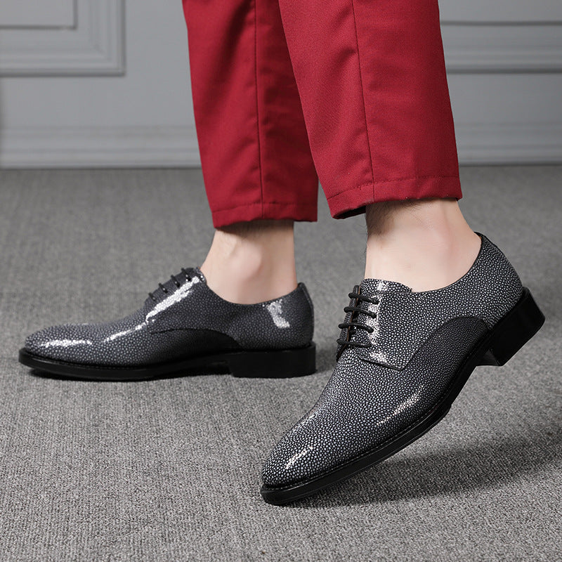 Black dress shoes with rhinestone details worn with red pants on a gray floor.