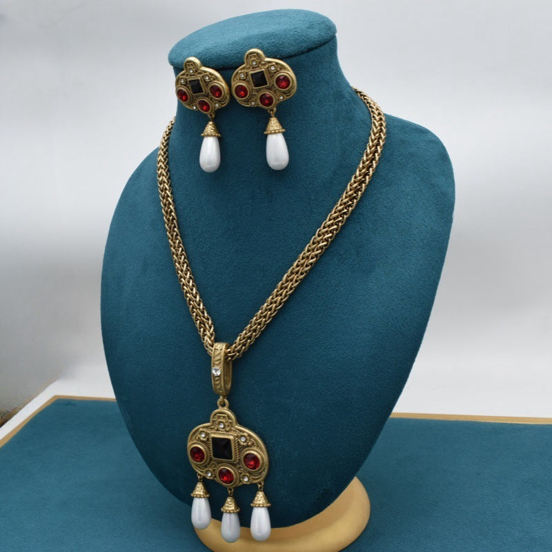 Gold necklace with red gemstones and white beads on a blue mannequin bust.