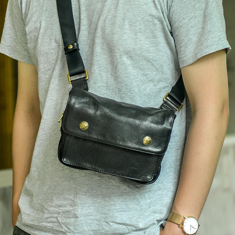 Person wearing a black leather crossbody bag with gold accents.