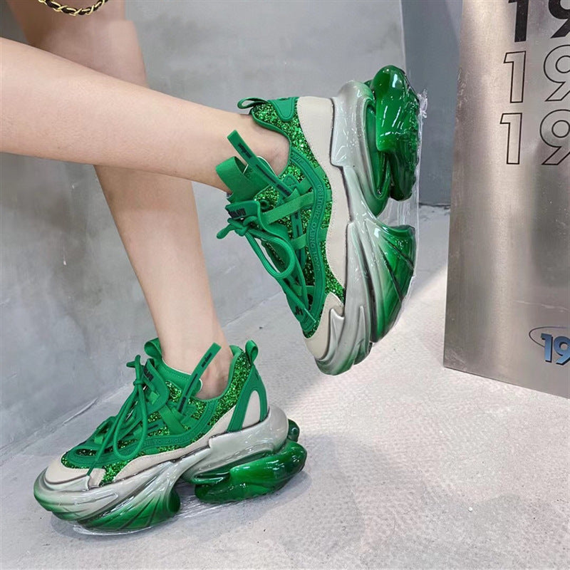 Green sneakers with transparent soles worn by a person, against a neutral background.