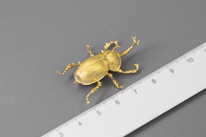 Gold beetle figurine next to a ruler on a gray background