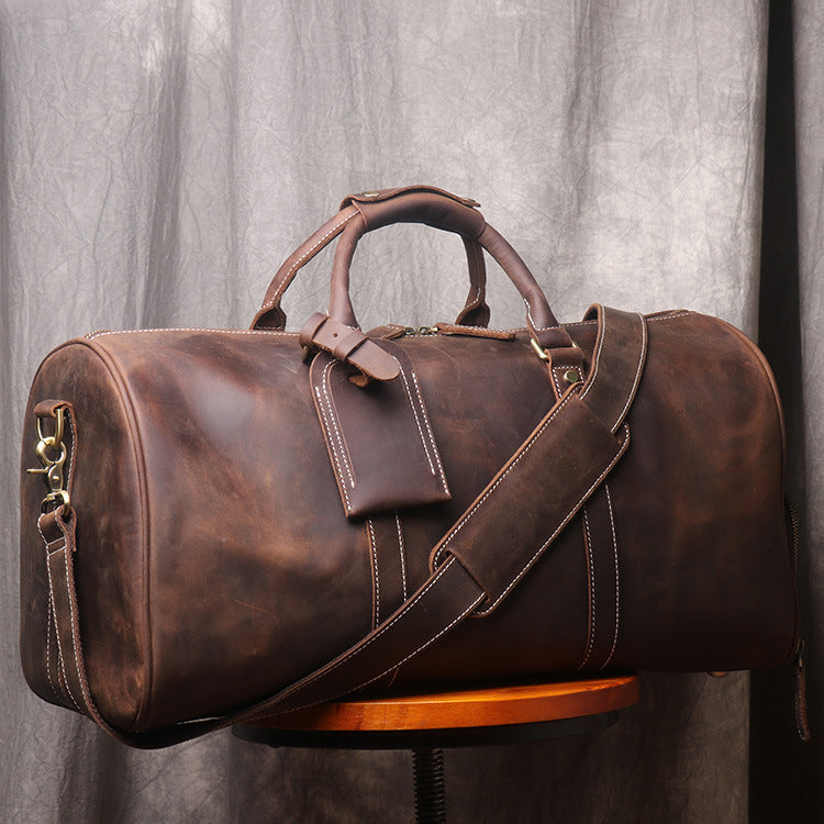 Brown leather duffel bag with a strap on a wooden stand against a gray curtain background
