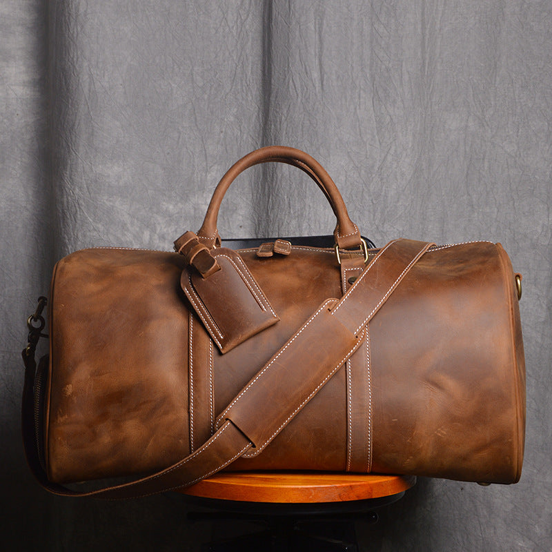 Brown leather duffel bag with a strap on a gray background