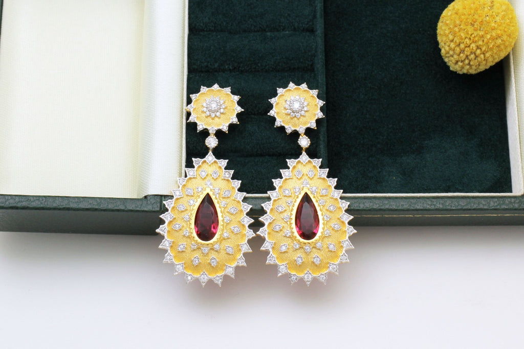 Gold earrings with red stones on a white surface
