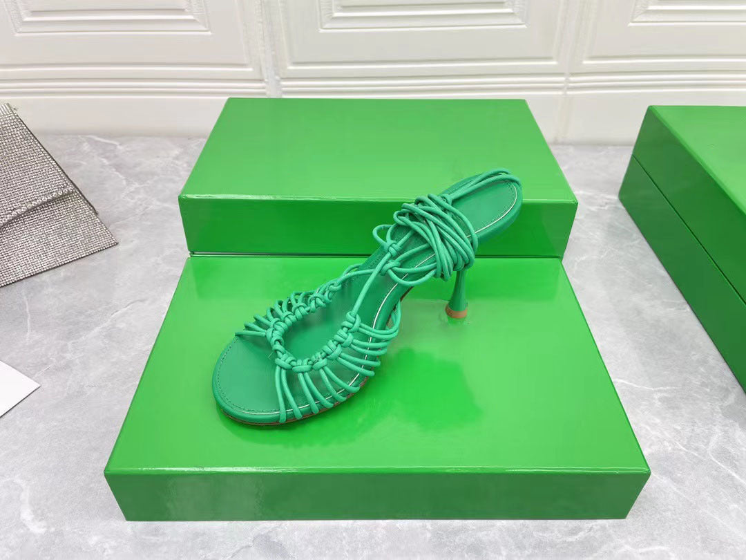 Green high-heeled sandal on a green box with a white background
