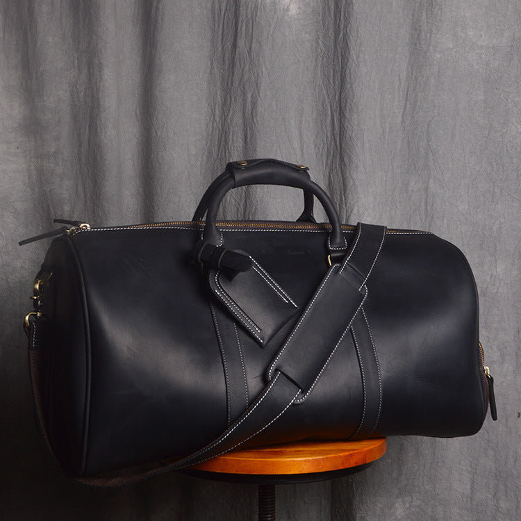 Black leather duffel bag on a wooden stand against a gray curtain background