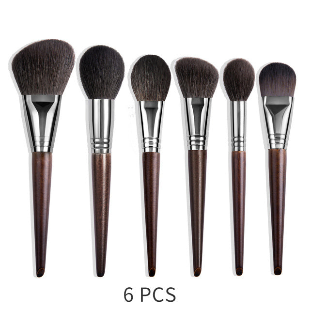 Set of six makeup brushes with brown handles and black bristles on a white background.
