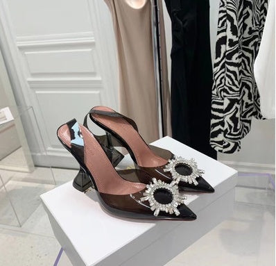 Black high-heeled shoes with decorative elements on a white platform.