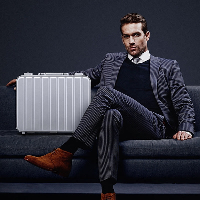 Man in a suit sitting on a couch with a silver suitcase