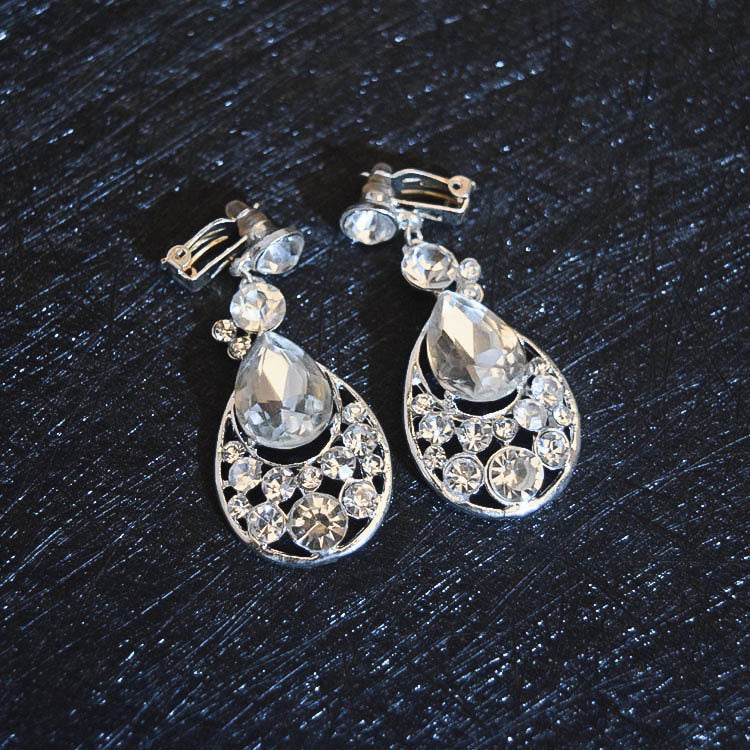 Pair of silver teardrop earrings with clear gemstones on a dark textured surface