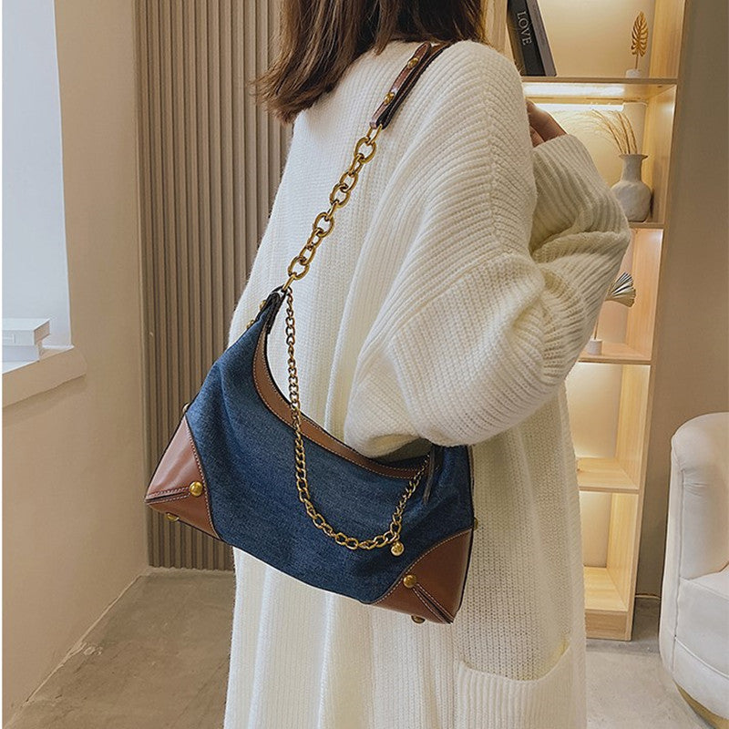 Person wearing a white sweater and holding a blue handbag with gold chain strap in an indoor setting.