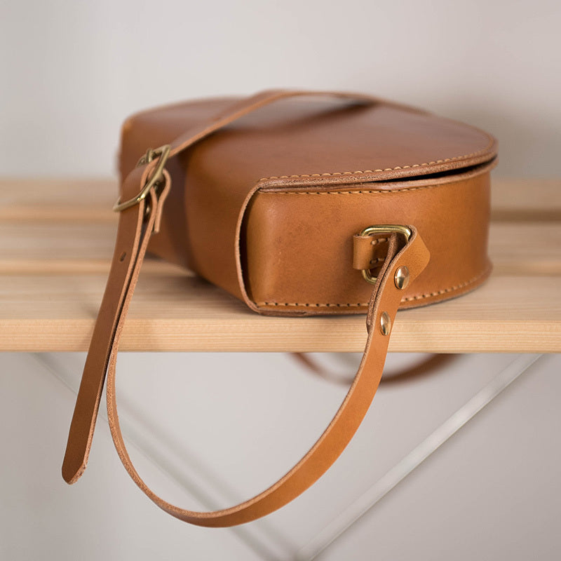 Brown leather handbag with a strap on a wooden shelf
