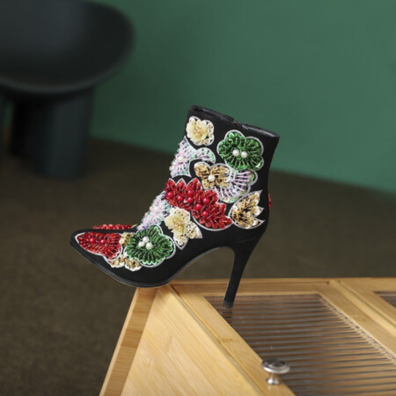 Decorative black high-heeled shoe with colorful floral embellishments on a wooden surface.