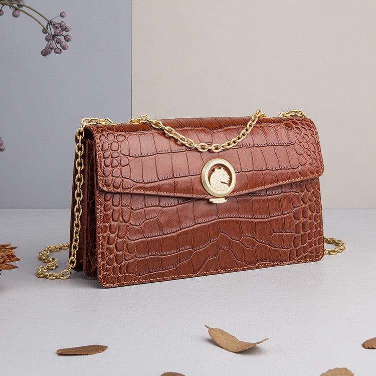 Brown crocodile-patterned handbag with gold chain on a light gray background