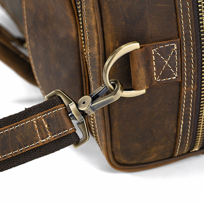 Close-up of a brown leather bag with a strap and metal buckle on a white background