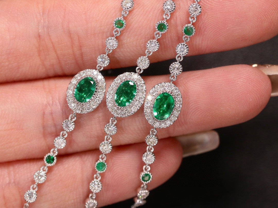 Silver necklace with emerald and diamond pendants held between fingers.