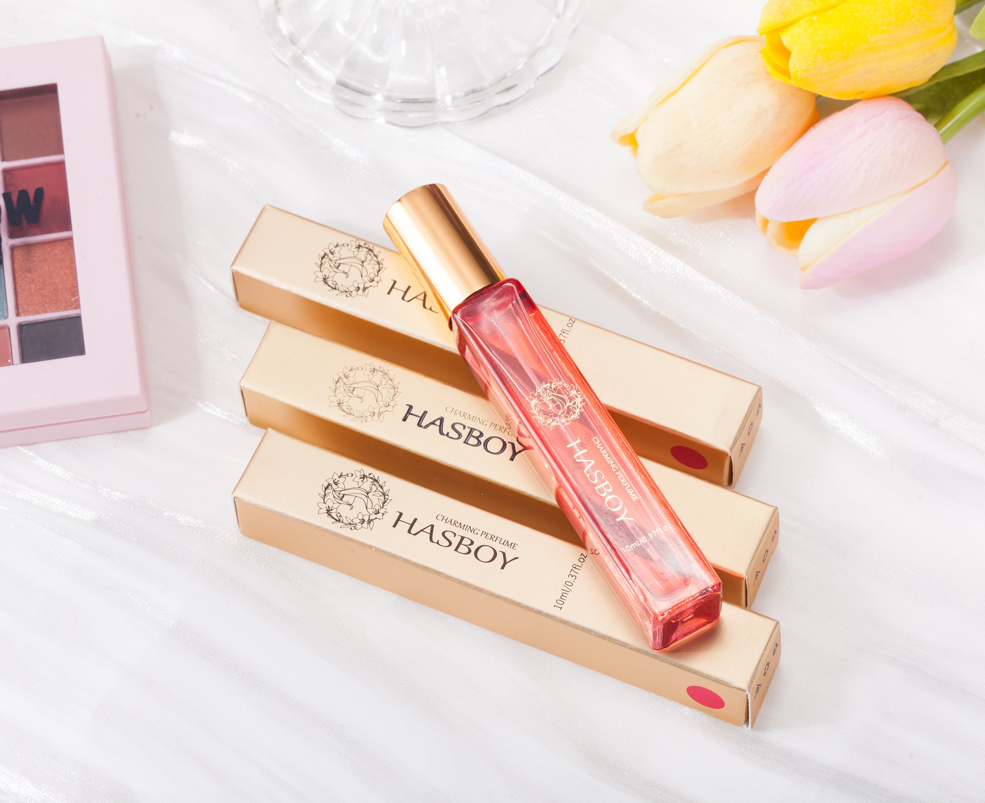 HASBOY lip gloss with packaging on a white surface with flowers in the background