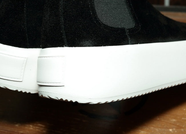 Close-up of a black sneaker with white sole on a wooden surface