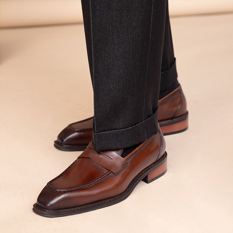 Brown dress shoes worn with black pants on a beige background