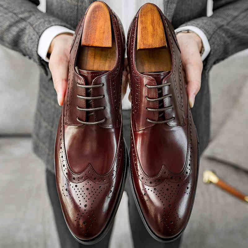 Brown leather dress shoes held by a person wearing a gray suit.