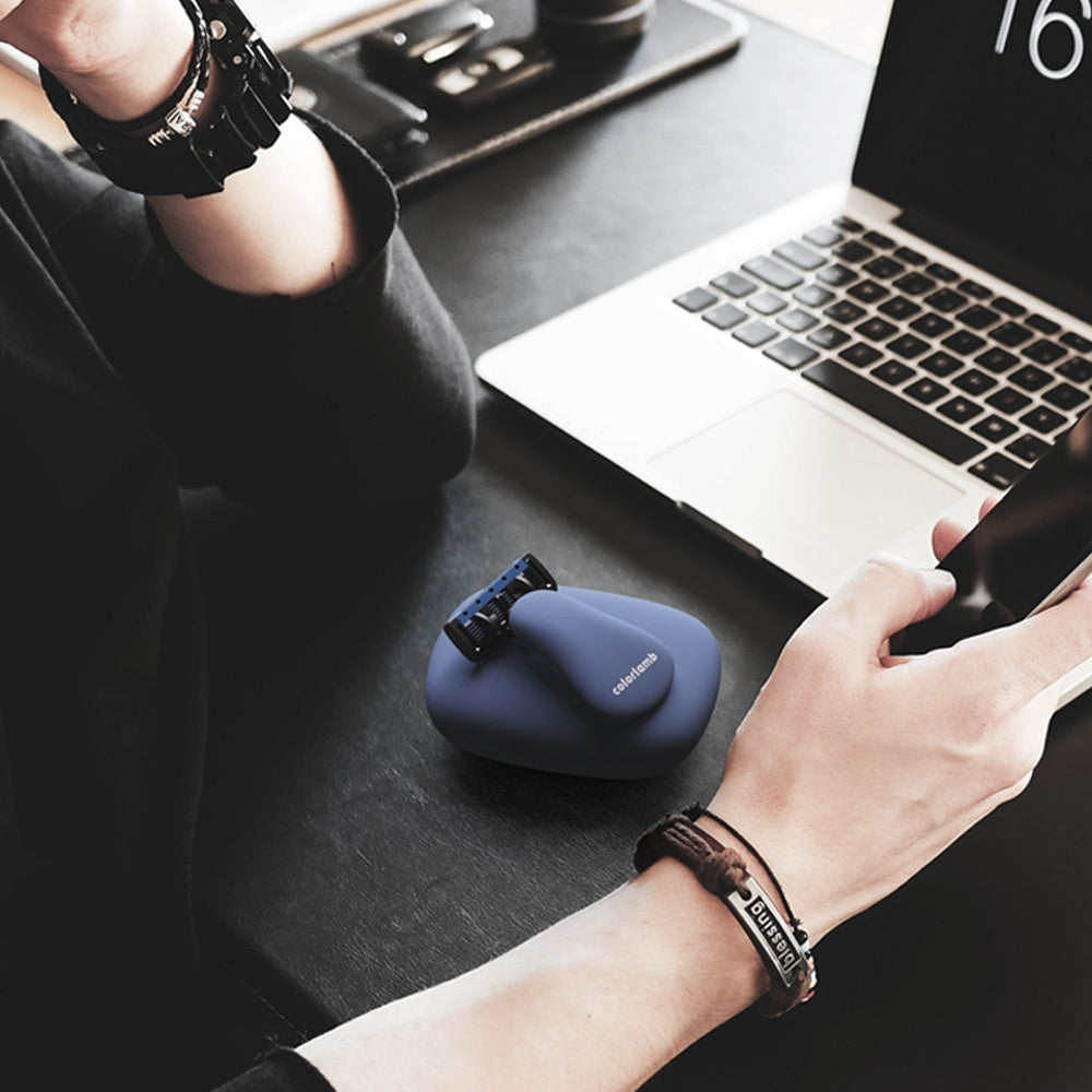 Person using a smartphone with a blue case on a desk next to a laptop.