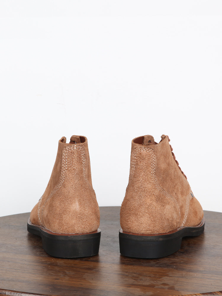 Pair of brown suede boots on a wooden surface with a white background