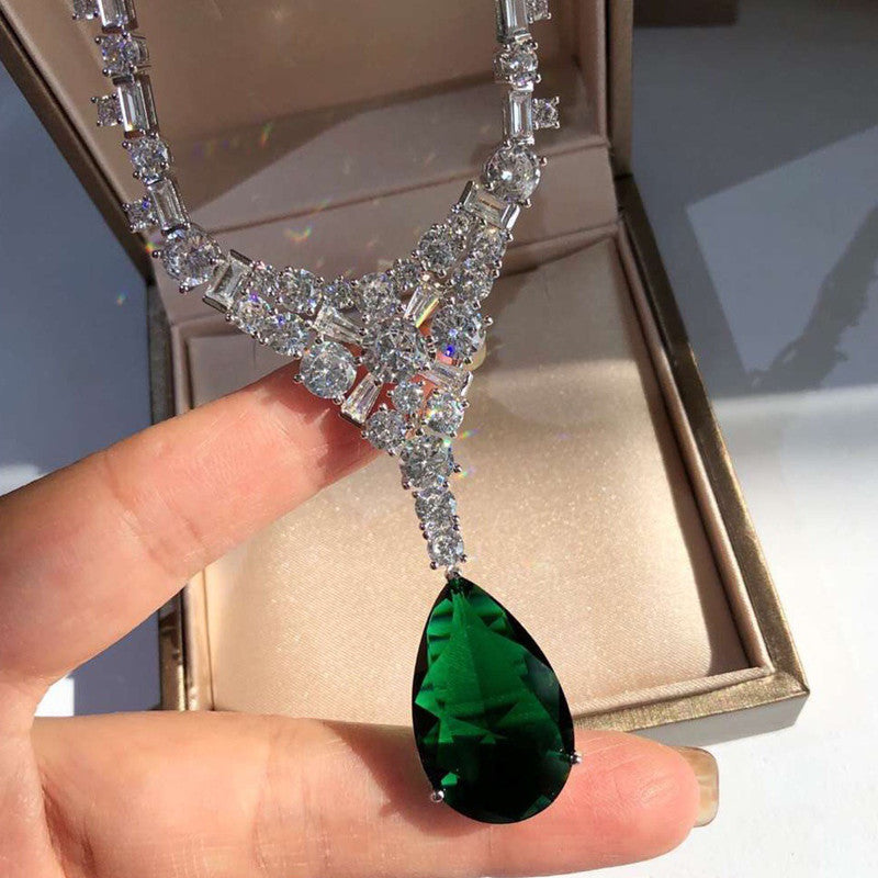Diamond necklace with a green teardrop pendant held by a hand.