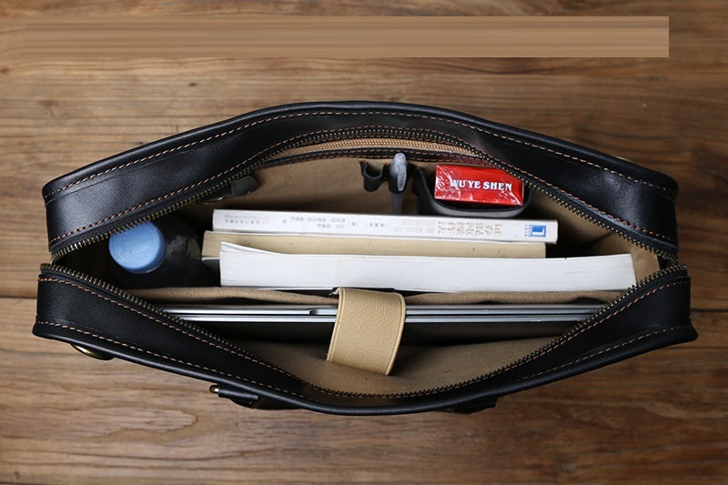 Black leather bag with items including books and a small bottle on a wooden surface