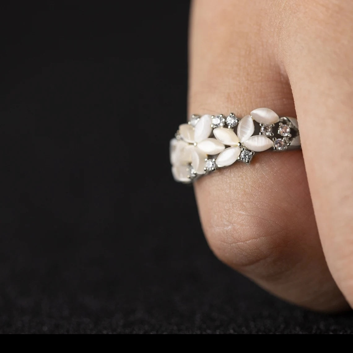 Close-up of a ring with floral design on a finger against a dark background