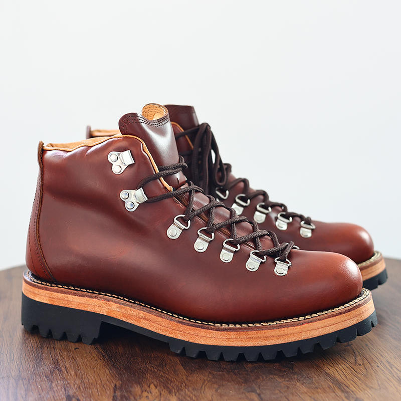Pair of brown leather hiking boots on a wooden surface with a light gray background